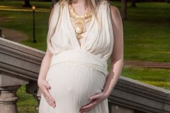 Pregnant woman standing sideways on outdoor stairs holding her tummy