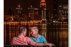 gay couple sitting on park bench by the river at night