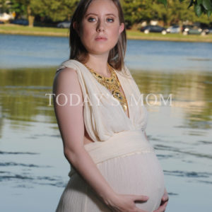 pregnant woman standing by a lake and looking at the camera