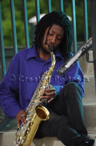 Lone saxophone player playing while sitting on outdoor stairs.